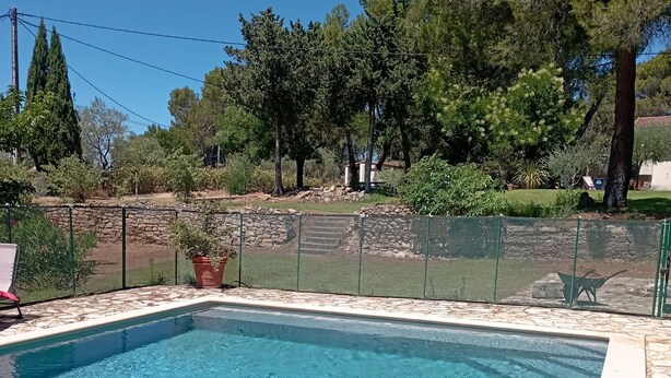 Piscina retangular com água azul cristalina, rodeada por um muro de pedra e uma cerca de metal.