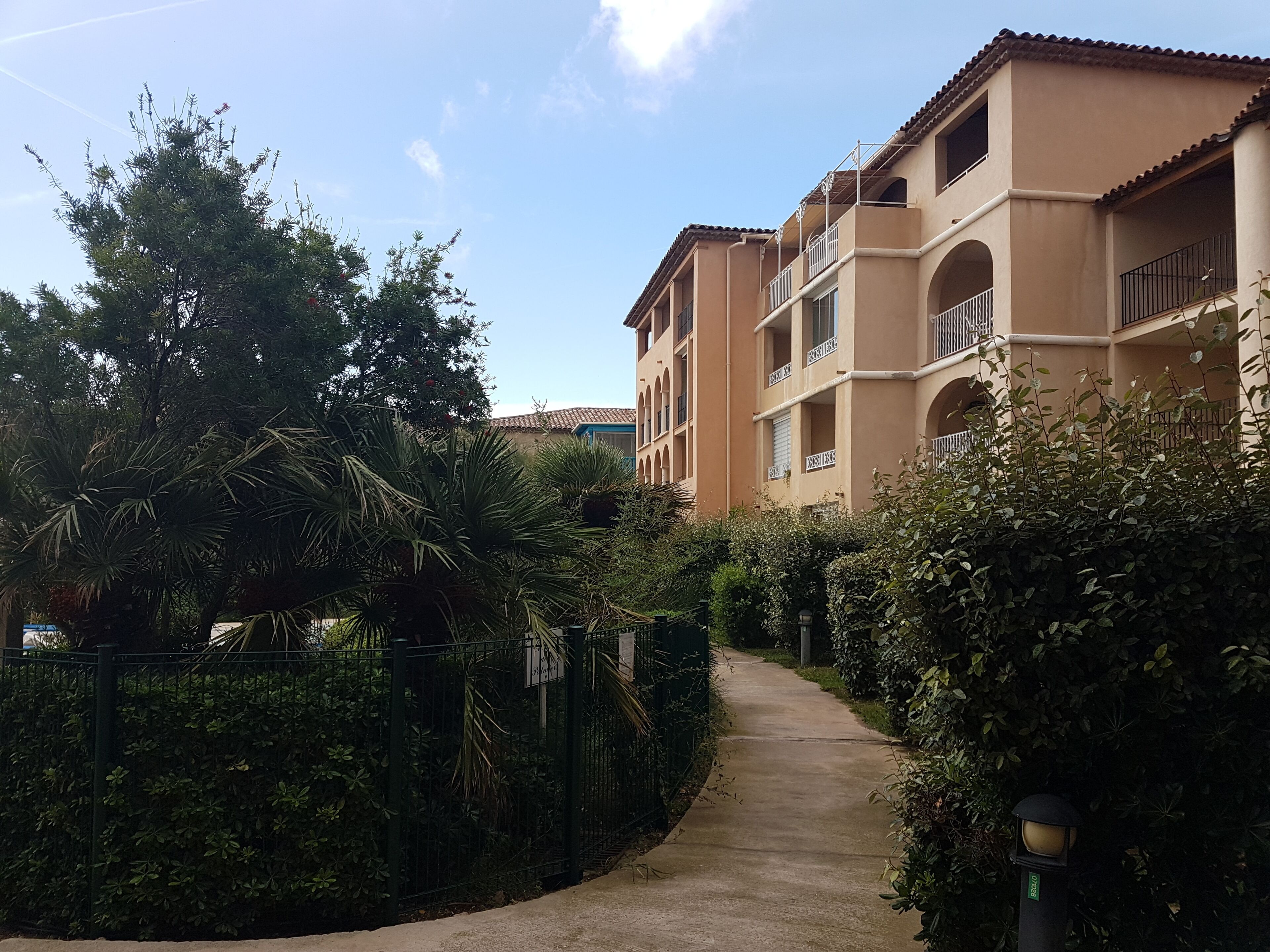 A pathway leading to a multi-story building with balconies and a tiled roof.