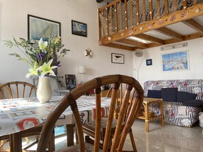 Un coin repas avec une table dressée pour deux personnes, une chaise en bois, un vase avec des fleurs et un canapé agrémenté de coussins à rayures.