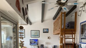 A spacious living area with a high ceiling, a ceiling fan, and a television. There are several wicker chairs and a dining table with a patterned tablecloth. - Grand Confort two-bedroom apartment with sea view and channel Near Sea (Agde)