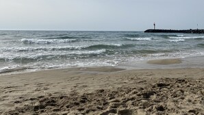 A beach with waves, a lighthouse, and a rocky breakwater. - Grand Confort two-bedroom apartment with sea view and channel Near Sea (Agde)