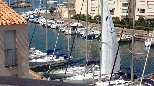 A marina with multiple sailboats docked, a building with a tiled roof, and a clear view of the water. - Grand Confort two-bedroom apartment with sea view and channel Near Sea (Agde)