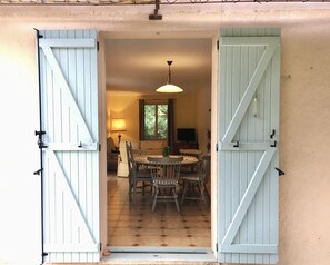 A dining area with a round table and chairs, a hanging light fixture, and a television in the background. - House with private pool in Provence in large wooded area *** (Flassans-Sur-Issole)