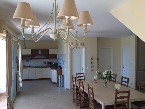 A spacious kitchen with modern appliances, a dining area with wooden chairs, and a chandelier.