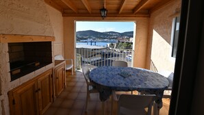 A balcony with a view of a body of water and hills, wooden ceiling, and a table with chairs. - Duplex, near the city center, on the left port exit (Port-Vendres)