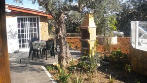 Eine Terrasse mit Tisch, Stühlen, einem Baum und einem Grill.