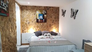 Ein Schlafzimmer mit einer Steinwand, einem Bett mit einem gemusterten Überwurf, zwei Kissen und einem Nachttisch mit einer Lampe.