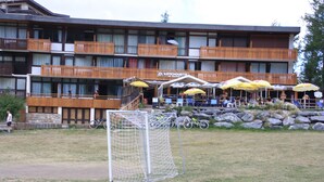 A hotel with multiple balconies, outdoor seating with umbrellas, and a visible goalpost. - Holidays close to the slopes. Pra-Loup 1600 (Uvernet-Fours)