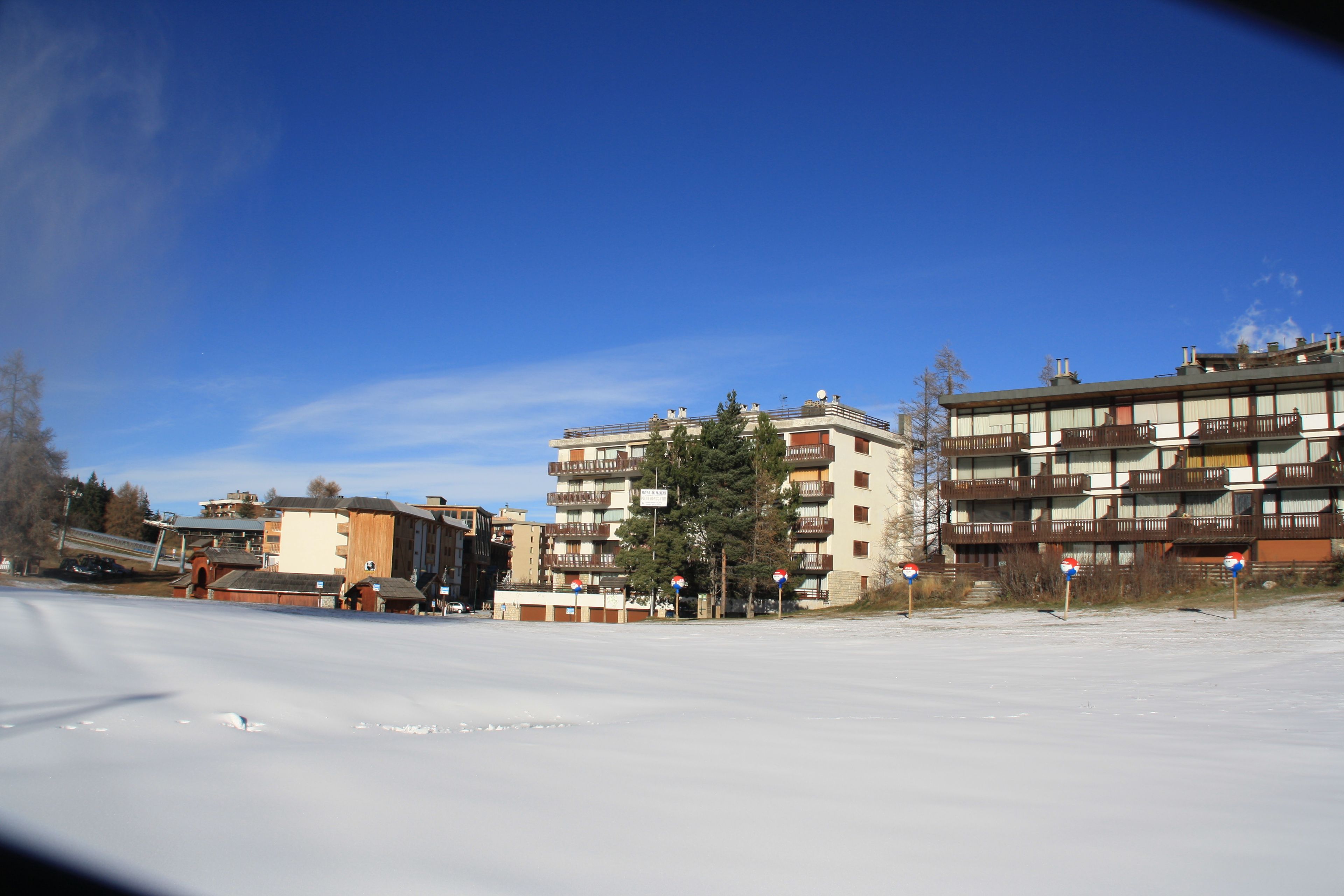 En snøklædt gade med høje bygninger, heriblandt et hotel med balkoner og en parkeringsplads.