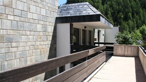 A modern building with a stone facade, a wooden deck, and a view of a forested hillside. - Holidays close to the slopes. Pra-Loup 1600 (Uvernet-Fours)