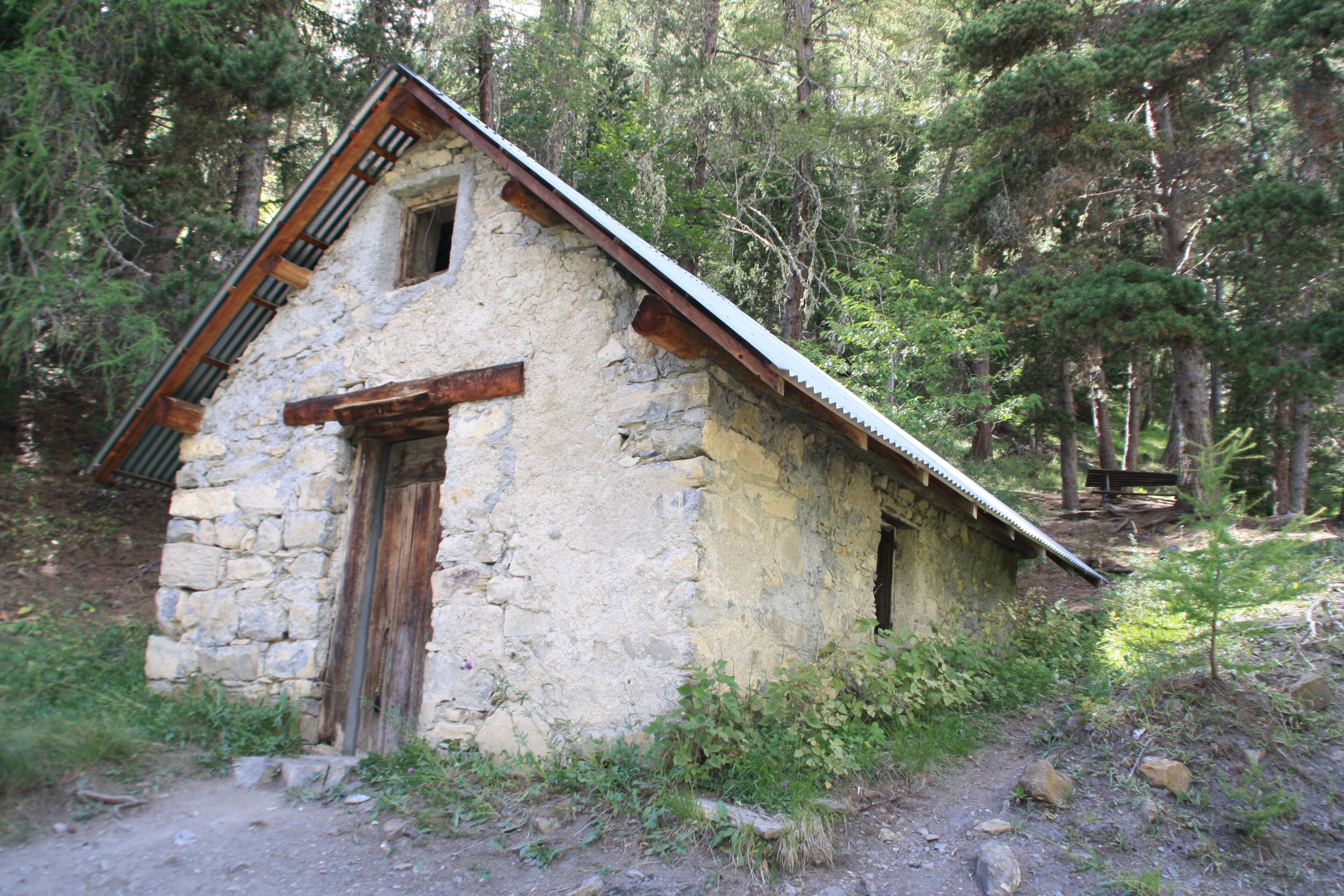 Une cabane rustique en pierre, avec un toit en pente, une porte en bois et une petite fenêtre.