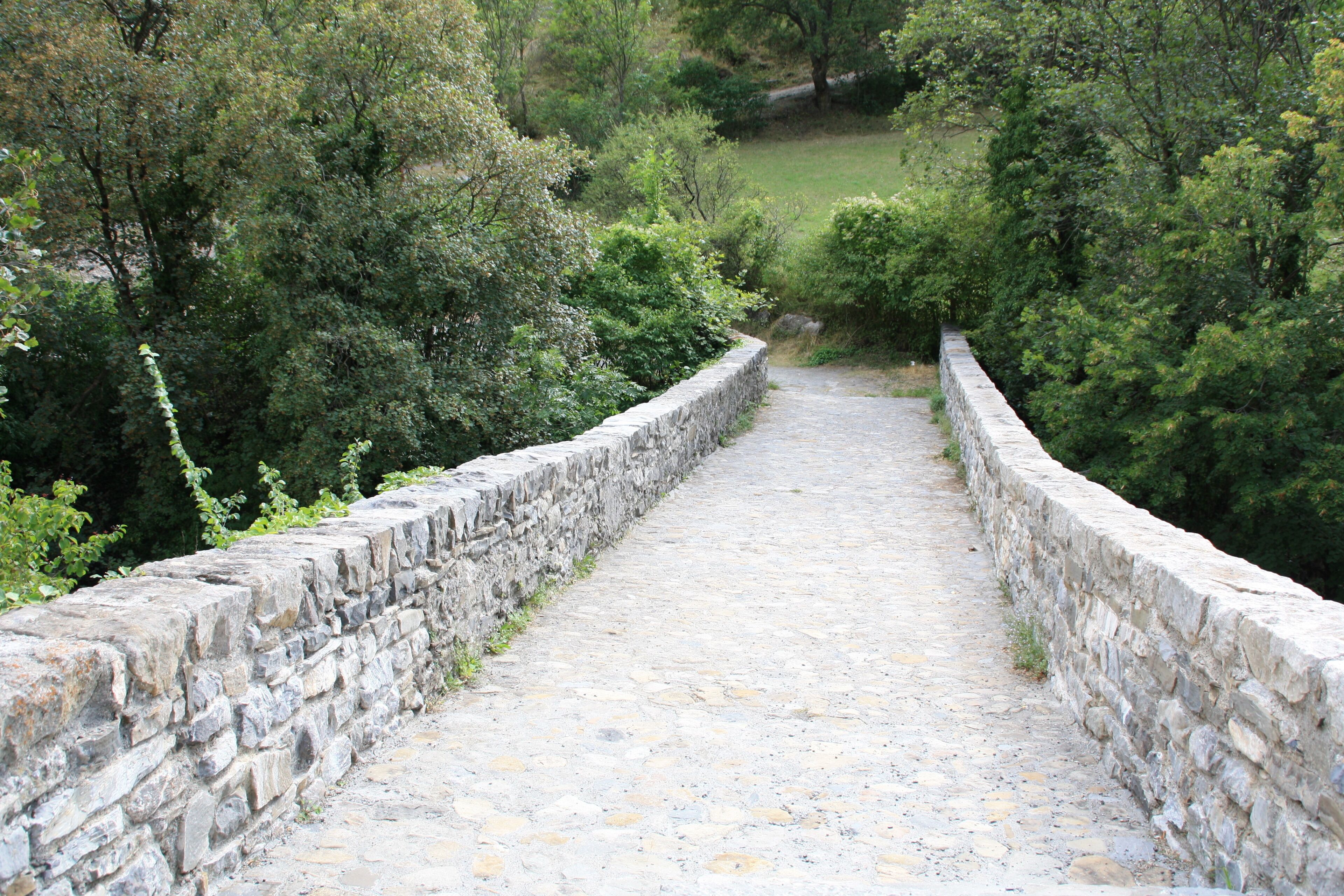 Un sendero de piedra bordeado por muros de piedra que atraviesa un área boscosa.