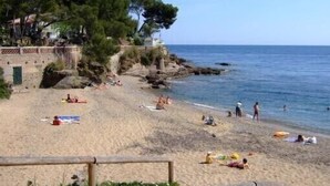 A beach with people sunbathing and swimming, a rocky shoreline, and a building with a green door. - Bastidon - Panoramic sea view - Quiet - Beach-300m - Air-conditioning - Private pk (Saint-Raphaël)