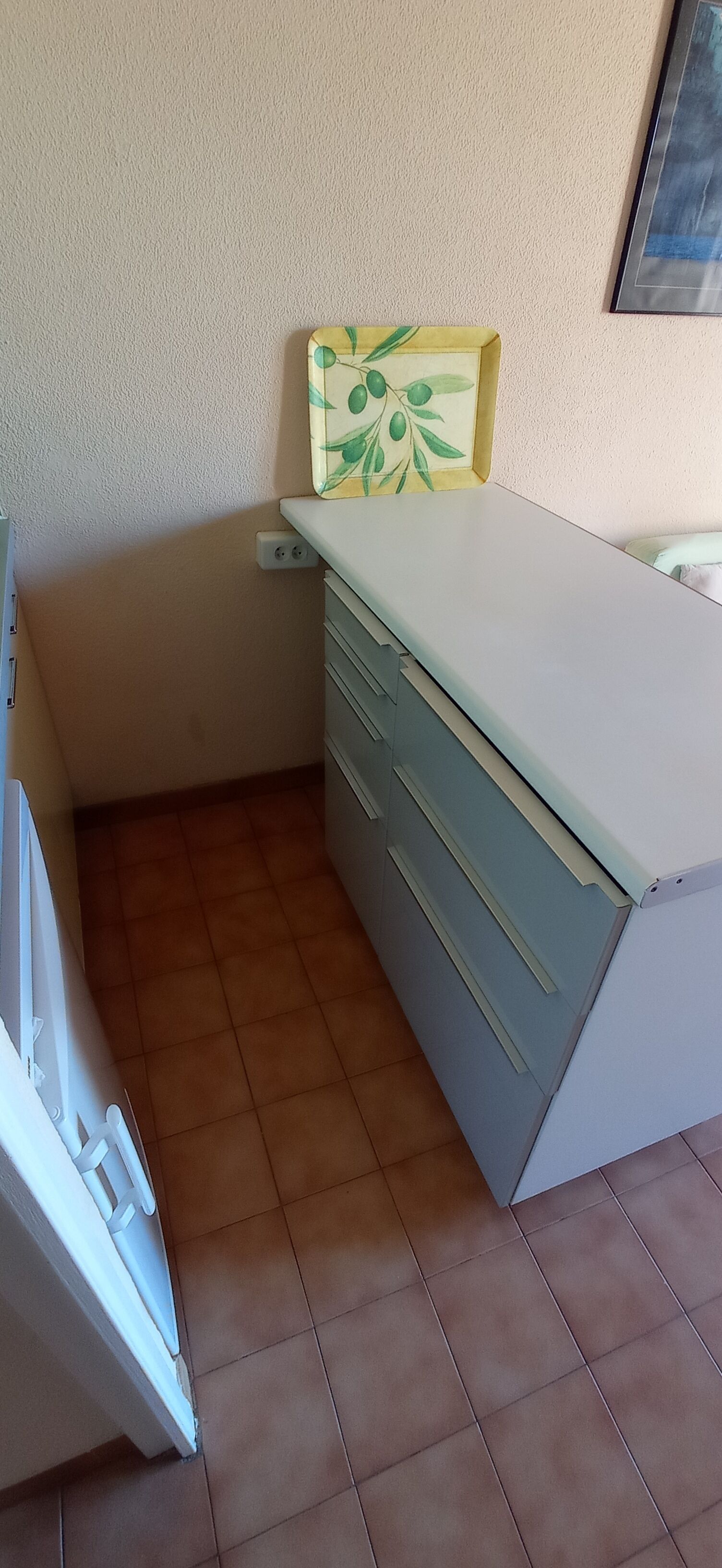 Een kleine kamer met een wit bureau, een stoel en een wandplank met een groen en geel ontwerp.