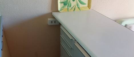 Een kleine kamer met een wit bureau, een stoel en een wandplank met een groen en geel ontwerp.