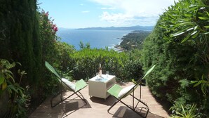 A patio with two green chairs and a table, overlooking a coastal landscape. - Bastidon - Panoramic sea view - Quiet - Beach-300m - Air-conditioning - Private pk (Saint-Raphaël)