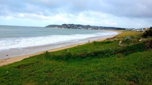 A coastal landscape with a beach, grassy foreground, and a distant town.