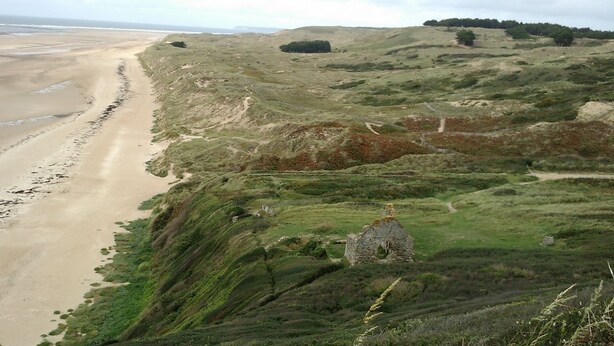 A coastal landscape with a sandy beach, rolling hills, and a stone structure.