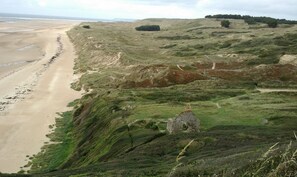 Eine Küstenlandschaft mit Sandstrand, sanften Hügeln und einer Steinstruktur.
