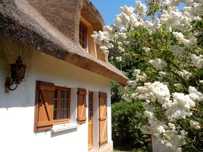 Une maison traditionnelle avec un toit de chaume, des volets en bois et une façade blanche.