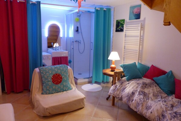 Une pièce comprenant un lit, une chaise, une table avec une lampe, un espace douche et une salle de bain.