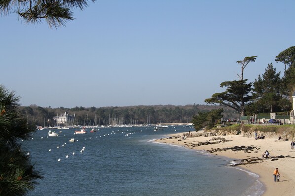 A coastal view with boats on the water, a sandy beach, and a forested area.