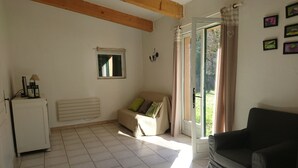 Een woonkamer met een betegelde vloer, een bank, een zwarte fauteuil, een radiator, een raam met gordijnen en een kleine tafel met een lamp.