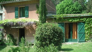 Een huis met twee verdiepingen, groene luiken, een schotelantenne en een tuin met paarse bloemen.