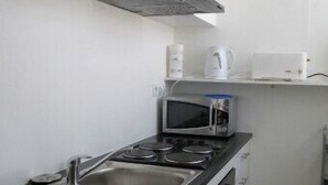 A compact kitchen with a stove, sink, and microwave. There is a kettle and a toaster on the countertop.
