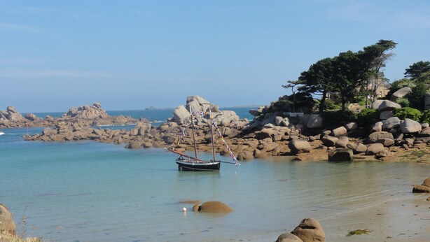 A coastal scene with a sailboat anchored near rocky shores.