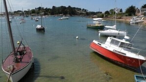 A marina with several boats docked, calm water, and a shoreline with buildings and vegetation.