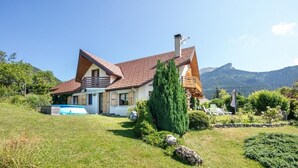Una casa de dos pisos con techo de tejas rojas, piscina y jardín bien cuidado.