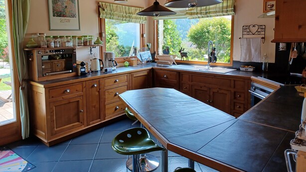 Cocina con armarios de madera, una isla grande, lámparas colgantes y vista a la vegetación exterior.