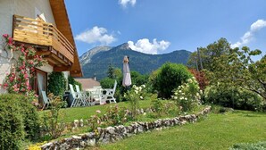 Una casa con balcón de madera, pared de piedra y jardín con flores y césped.