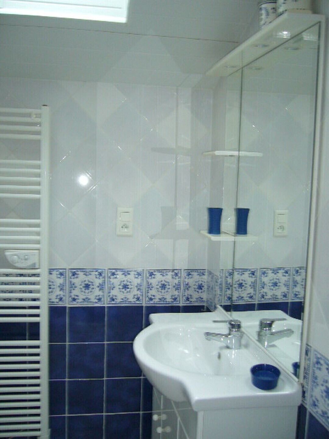 A bathroom with a white sink, blue tiles, and a mirror.