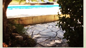 Una piscina con sillas de descanso, rodeada de árboles y un sendero de piedra.