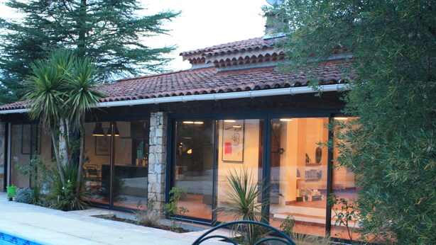 Zona de piscina con terraza de baldosas, una silla de metal y un edificio con techo y puertas de vidrio.