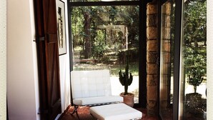 Una habitación con un banco acolchado blanco, una lámpara colgante y vistas a un jardín a través de amplias puertas de vidrio.