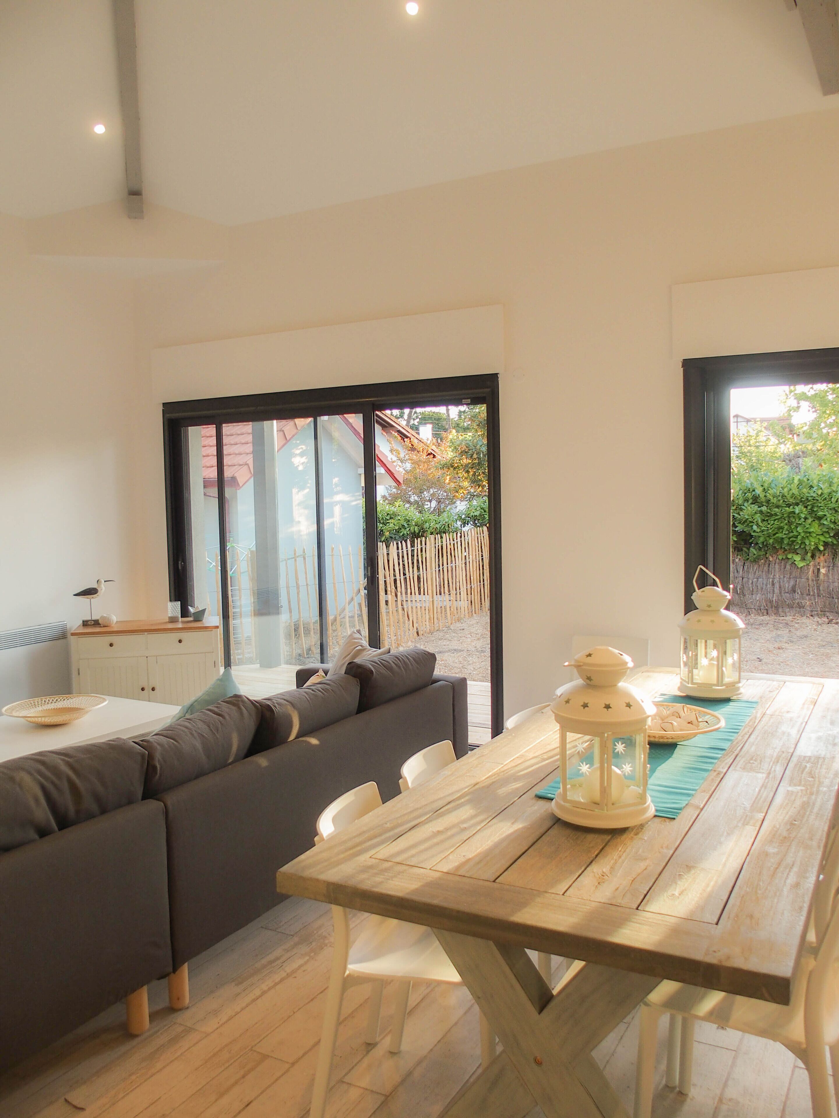 Ein modernes Wohnzimmer mit einem Holztisch, einem grauen Sofa und Blick auf einen Garten durch große Glasfenster.