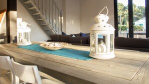 Een houten eettafel met witte stoelen, een blauwe placemat en twee witte lantaarns. Achtergrond toont een trap.