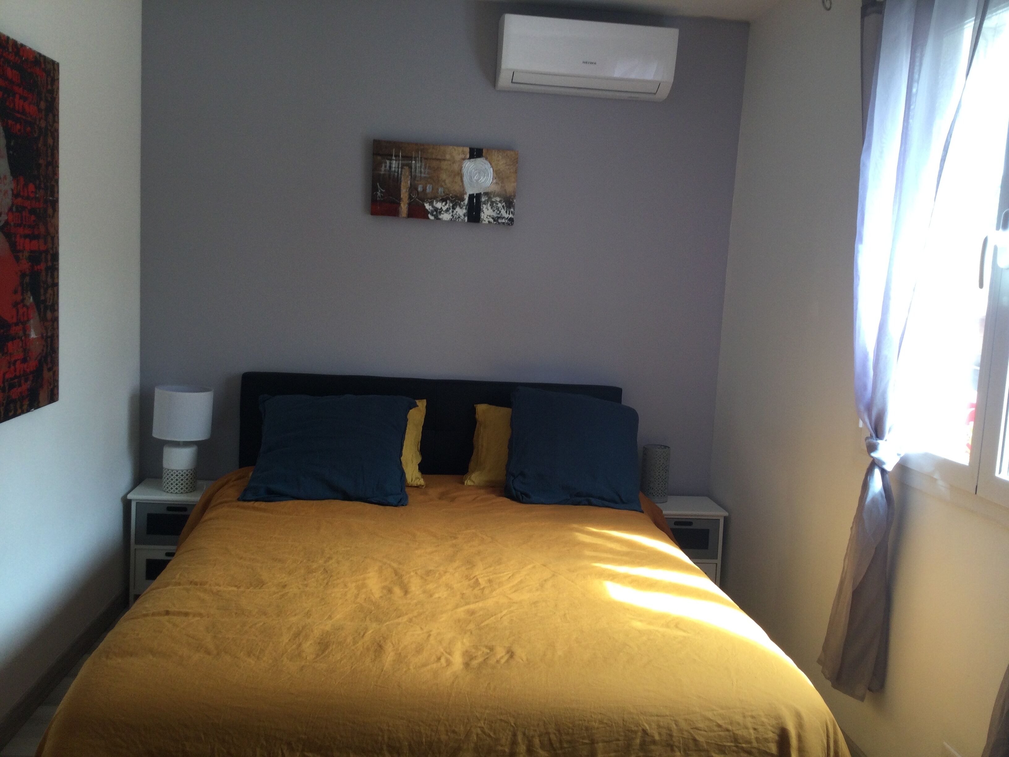 Une chambre d’hôtel avec un lit, une table de chevet, une lampe, un climatiseur et un tableau au mur.