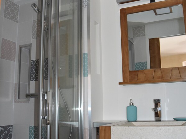 Une salle de bain dotée d’une douche à paroi de verre, d’un miroir à cadre en bois et d’un plan de toilette blanc avec un distributeur de savon.