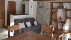 Un salon moderne avec un canapé gris, des chaises en bois, une table à manger en bois et un mur d’accent en pierre.