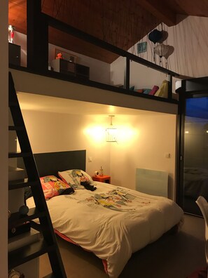 A bedroom with a bunk bed, a bedside table with a lamp, and a window with a view.