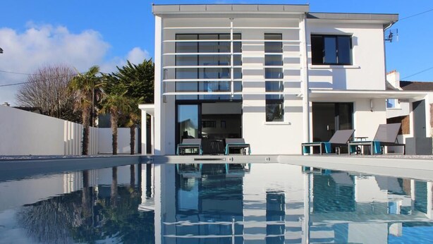 Ein modernes, zweistöckiges Haus mit einem Schwimmbecken davor.