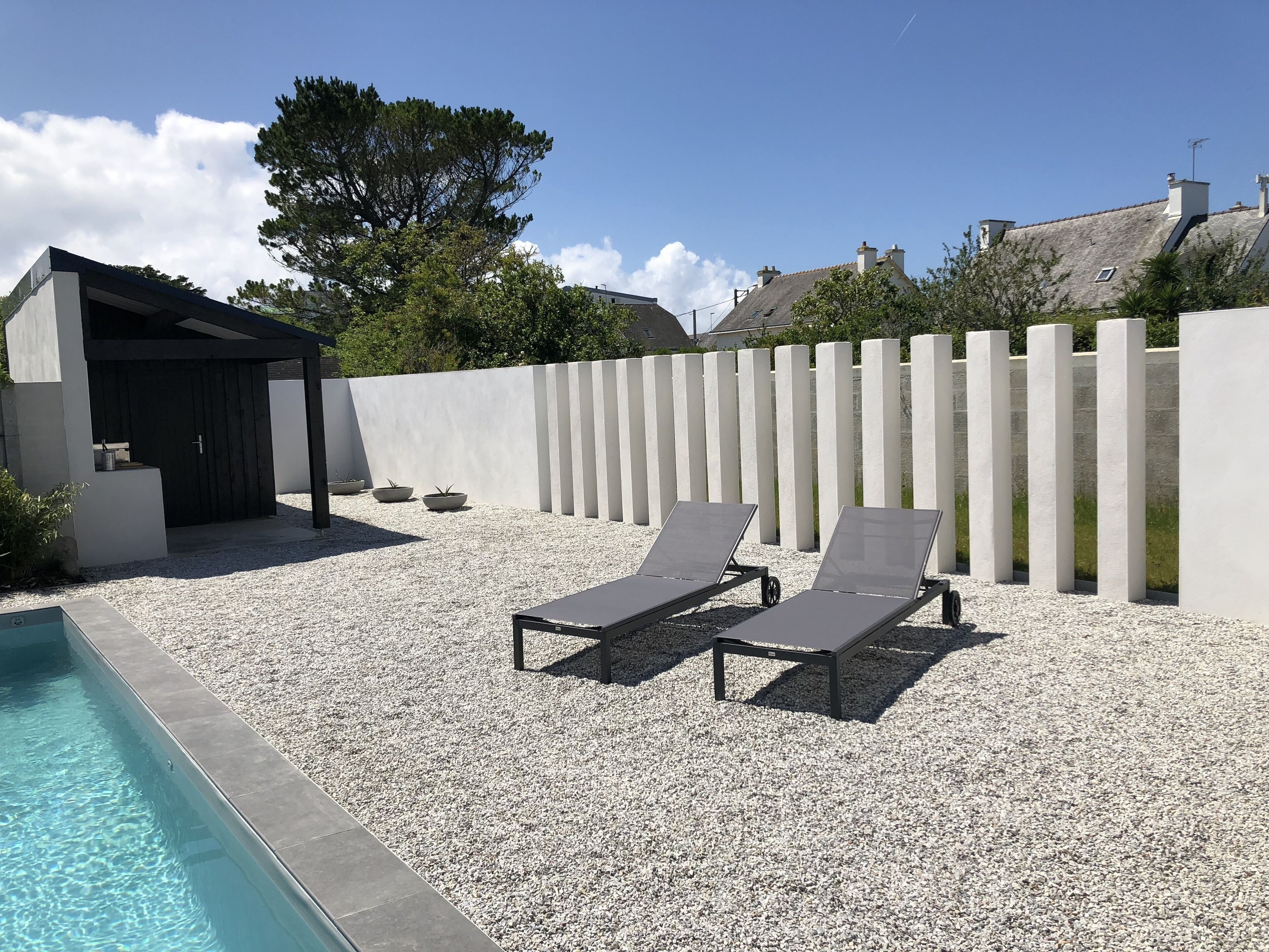 A poolside area with a pergola, two lounge chairs, and a small outdoor kitchen.