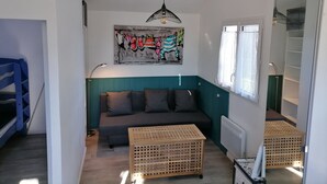 Ein Wohnzimmer mit einer Couch, einem Holztisch, einem Bild an der Wand und einem Fenster mit Vorhängen.