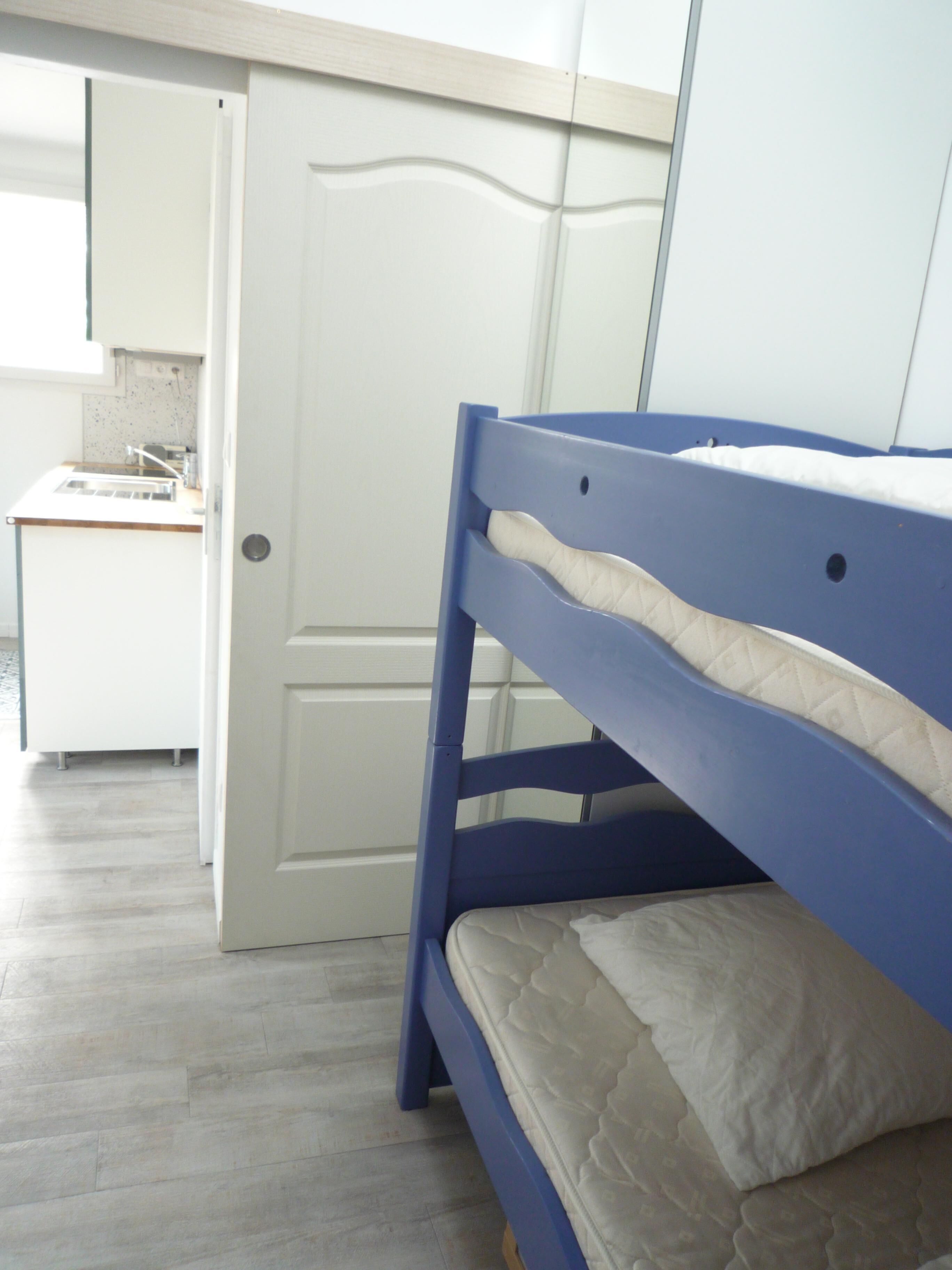 A bunk bed with a mattress and a headboard, a white door, and a kitchen area with a countertop and cabinets.