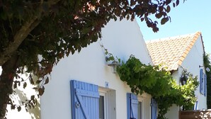 Ein weißes Gebäude mit blauen Fensterläden, einer Holzterrasse und einem Garten.