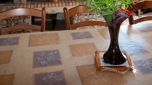 A dining area with a table set for two, a vase with flowers, a fireplace, and a clock on the wall.